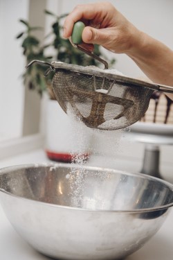 A photograph of someone sifting flour into a bowl.