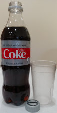 A full bottle of Diet Coke beside an empty glass.